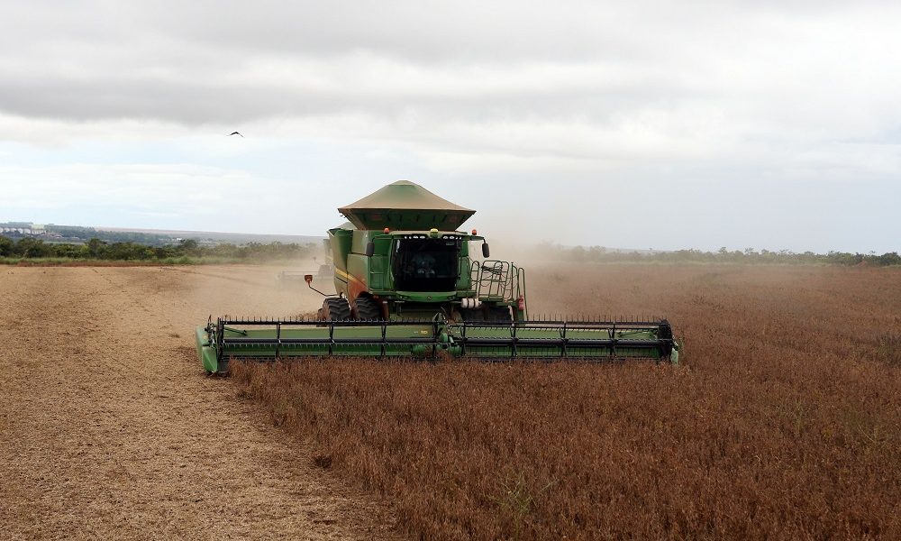 Com o céu nublado no horizonte, trator passa fazendo a colheita de soja em fazenda