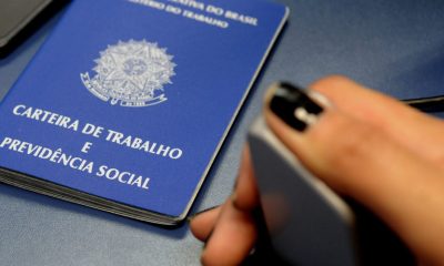 Mão pressiona aparelho de captação de digital ao lado de uma carteira de trabalho