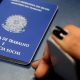 Mão pressiona aparelho de captação de digital ao lado de uma carteira de trabalho
