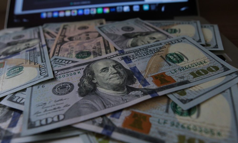 Notas de dólar sobrepostas e, no fundo, a base de um notebook