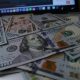 Notas de dólar sobrepostas e, no fundo, a base de um notebook