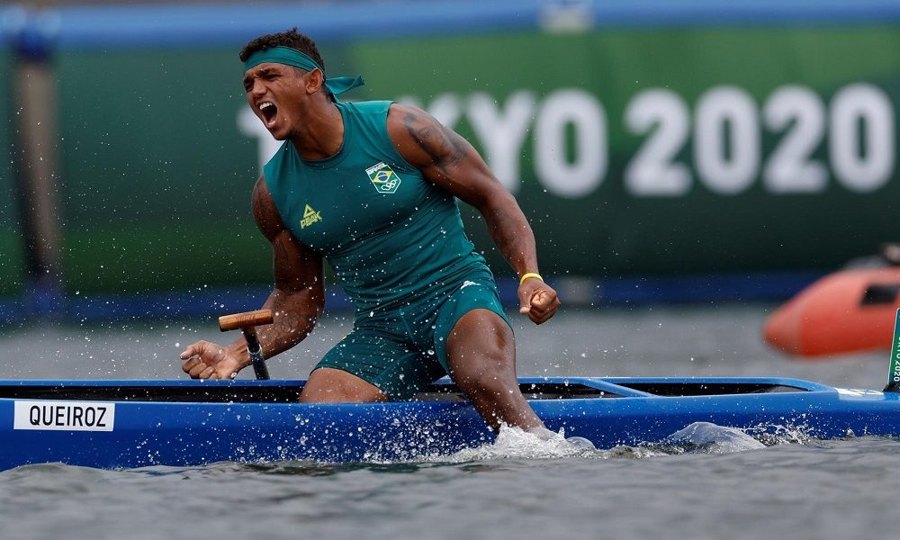 Sentado na canoa, mas com as pernas na água, Isaquias, vestido de verde, solta um grito após ganhar o ouro