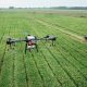 Imagem aérea mostra um drone sobrevoando um extenso campo agrícola, por onde passa um trator