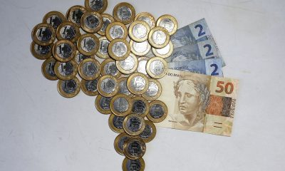 Moedas de R$ 1 formam o mapa do Brasil; do lado direito, há três notas de R$ 2 e uma de R$ 50